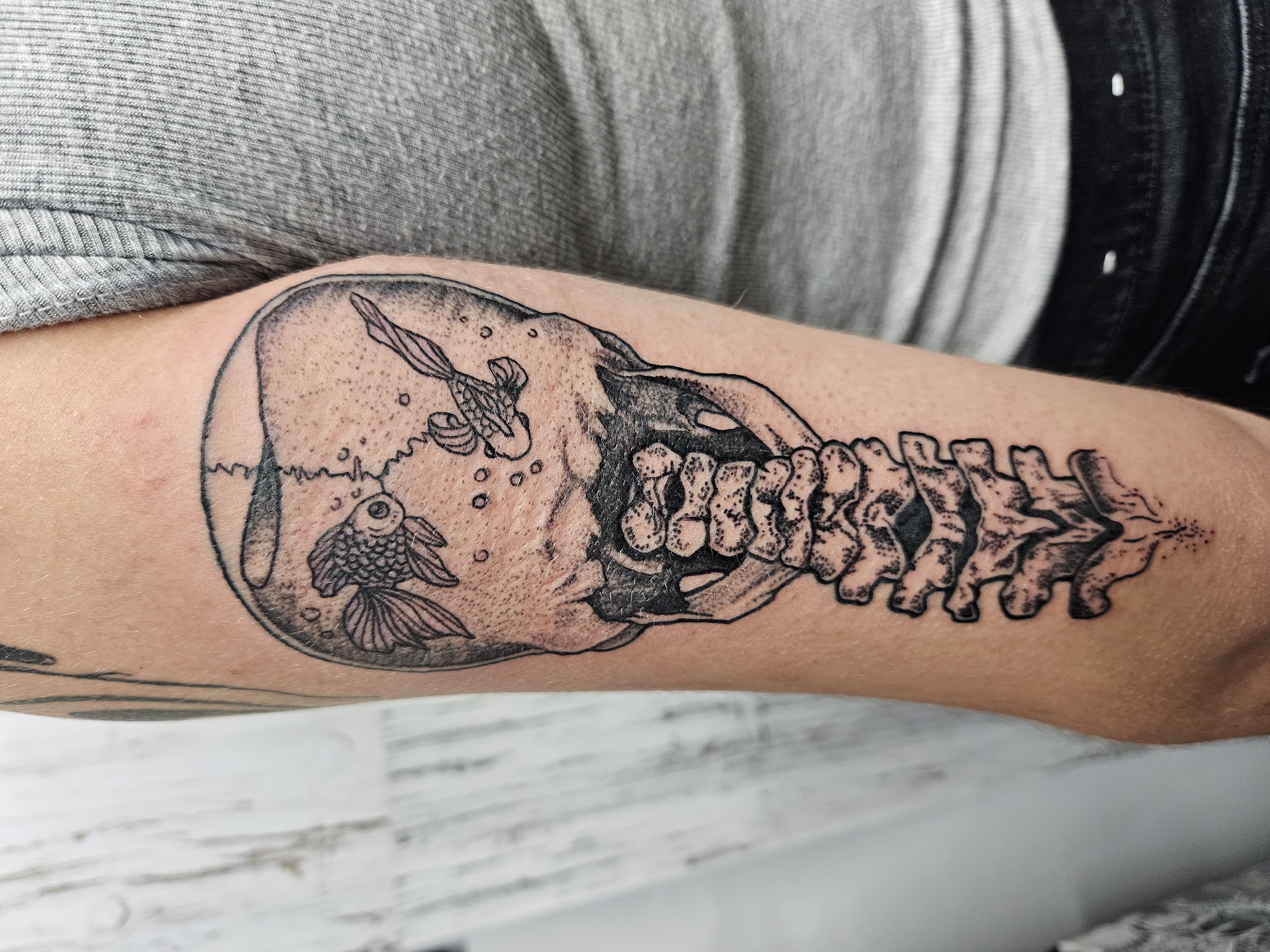 Skull and spine aquarium tattoo in black and grey.